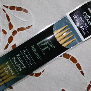 Puede incluir: Un paquete de cuatro agujas de tejer de bambú Takumi con puntas cónicas. Las agujas miden 5,0 mm (tamaño US 8) y 12,5 cm de largo. El paquete es negro con texto blanco y el logotipo de Clover.