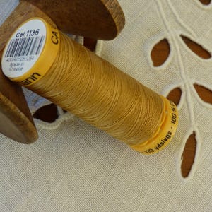May include: A spool of brown embroidery thread wound on a wooden bobbin. The label on the spool reads "Col. 1136" and "110 yds/vgs - 100 m".