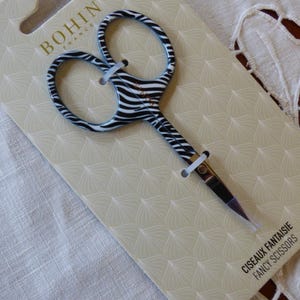 Pode incluir: Tesoura de fantasia BOHIN France com um design de estampa de zebra em preto e branco. Apresentada em um cartão creme com um padrão decorativo. O texto "CISEAUX FANTAISIE FANCY SCISSORS" está impresso no cartão.