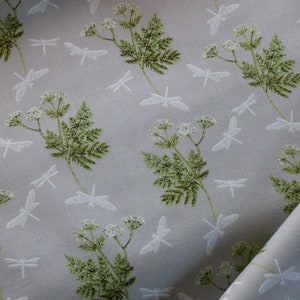Könnte beinhalten: Ein hellgrauer Stoff mit einem sich wiederholenden Muster aus weißen Libellen und grünen Farnen. Der Stoff hat eine subtile Textur.