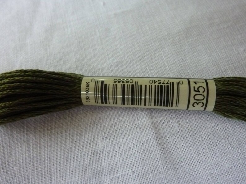 Peut inclure: Une bobine de fil &agrave; broder vert fonc&eacute; avec une &eacute;tiquette blanche sur laquelle est inscrit "3051" et un code-barres. L'&eacute;tiquette comprend &eacute;galement les num&eacute;ros "077540", "05985" et "3921036K".