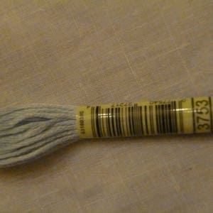 Op de afbeelding: Een klosje lichtblauwe borduurgaren met een geel label waarop "DMC 3753" staat.