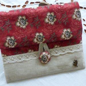 Peut inclure: Une pochette en tissu rouge avec un motif floral et un rabat en lin beige. La pochette est ornée d'une bordure en dentelle et d'un bouton décoratif.