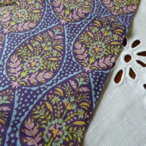 Könnte beinhalten: Nahaufnahme eines gemusterten Stoffes mit einem Paisley-Design in Lila, Blau, Gelb und Rosa. Der Stoff liegt neben einem weißen Stoff mit Lochmuster.