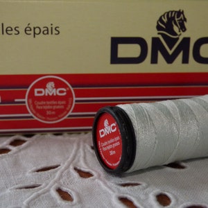 Könnte beinhalten: Eine weiße DMC Stickgarnrolle mit schwarzem Plastikdeckel. Die Rolle ist mit "Coudre textiles épais Par textiles grossis 30m" beschriftet.
