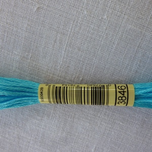 Op de afbeelding: Een klosje lichtblauwe borduurgaren met een geel label waarop "3846" staat.
