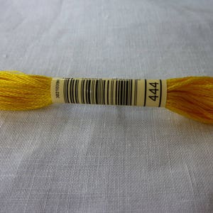 Op de afbeelding: Een spoel met felgele borduurgaren met een wit label waarop "DMC 3021 444" staat.