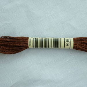 Op de afbeelding: Een streng bruin borduurgaren, kleur 898, met een barcode label. Het garen is strak opgerold en lijkt gemaakt van een zacht, glanzend materiaal. De achtergrond is een lichte, getextureerde stof.