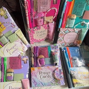 May include: Five gift sets packaged in clear plastic, each containing a set of prayer cards, a small hand sanitizer, a tube of hand cream, a beaded bracelet, and various pens or highlighters. Each set features distinct color themes and religious text.