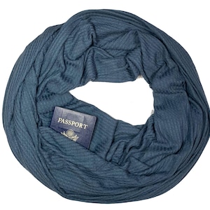 May include: A blue infinity scarf with a hidden pocket, holding a passport. The scarf is made of a soft, ribbed fabric. The passport is visible in the pocket, with the word "PASSPORT" clearly displayed.