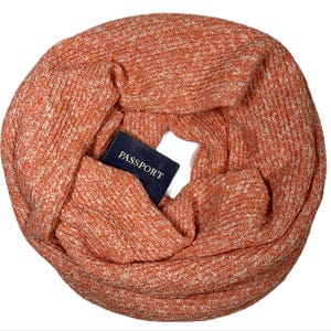 May include: A soft, orange and white knit infinity scarf. The scarf is folded in half and a blue passport is tucked inside.