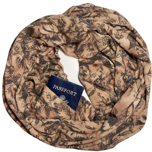 May include: A tan and gray infinity scarf with a floral pattern. A blue passport is visible in the scarf's pocket. The scarf is made of soft fabric and is designed for travel.