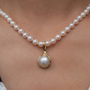 May include: A white pearl necklace with a single large pearl pendant. The necklace is made of small, round pearls and has a gold clasp.