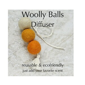May include: A Woolly Balls Diffuser with three felt balls in cream, gold, and orange, connected by a white string and tassel. The text reads "reusable & ecofriendly" and "just add your favorite scent."
