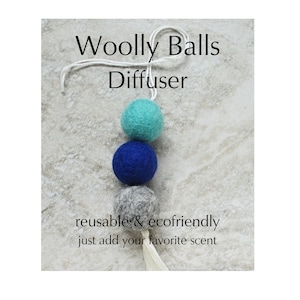 May include: A Woolly Balls Diffuser with three felt balls in teal, blue, and gray, suspended by a white string. The text reads "reusable & ecofriendly just add your favorite scent."