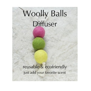 May include: A Woolly Balls Diffuser featuring three colorful felt balls in pink, green, and yellow, suspended by a white string. The text reads "reusable & ecofriendly just add your favorite scent."