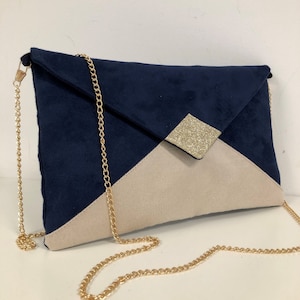 Puede incluir: Un clutch de sobre azul marino y beige con una correa de cadena dorada. La solapa delantera del clutch tiene un acento de brillo dorado.