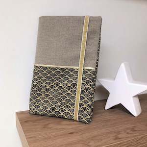 Può includere: Una pochette in tessuto beige e nero con un nastro dorato. La pochette ha un motivo geometrico di onde nere e dorate.