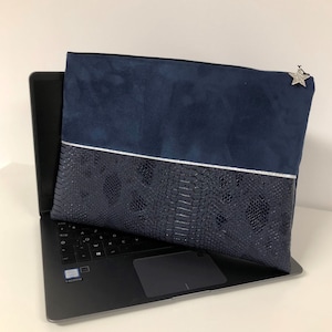 Peut inclure: Une pochette pour ordinateur portable de couleur bleu marine avec un charme étoile argenté. La pochette a un dessus en daim et un bas en faux cuir de serpent avec une bande argentée.