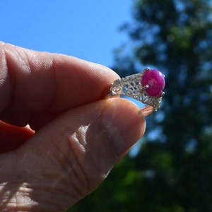 May include: A silver ring featuring a pink ruby gemstone set in a delicate filigree design.