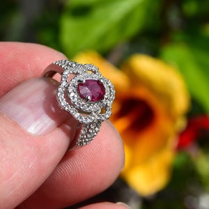 Peut inclure: Une bague en argent avec une pierre ovale rouge entourée de petites pierres blanches.