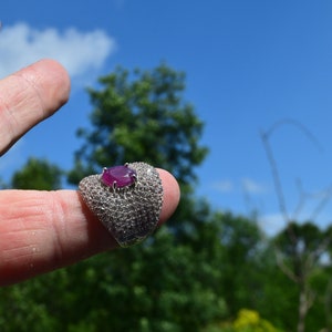 May include: A silver ring featuring a large oval ruby gemstone surrounded by smaller white gemstones.