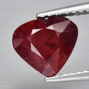 May include: A heart-shaped ruby gemstone with a deep red colour. The gemstone is faceted and has a polished finish.