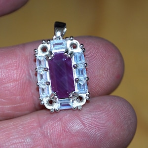 May include: A silver pendant featuring a purple gemstone set within a border of clear cubic zirconia stones.