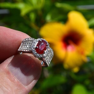 May include: A silver ring featuring a large oval ruby gemstone, surrounded by smaller diamonds. The ring is set in a delicate, intricate design.