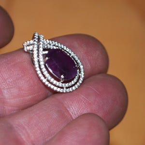 May include: A silver pendant featuring a large, oval-shaped amethyst gemstone set within a double row of smaller, clear gemstones.