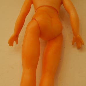 May include: A peach-colored plastic doll torso with arms and legs. The figure features a smooth, molded surface with defined joints at the shoulders and hips, showing a simple, unadorned human-like form without clothing or facial features.