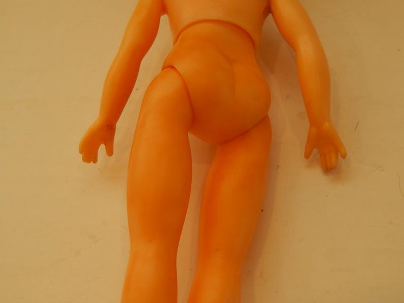 May include: A peach-colored plastic doll torso with arms and legs. The figure features a smooth, molded surface with defined joints at the shoulders and hips, showing a simple, unadorned human-like form without clothing or facial features.