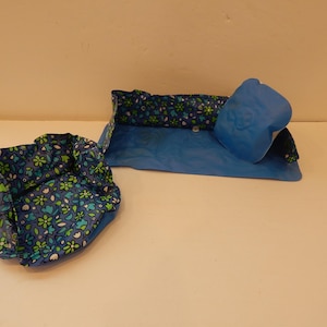 May include: A blue and floral patterned pet bed set. The set includes a round bed, a rectangular bed, and a pillow. The floral pattern features green and white flowers on a dark blue background.