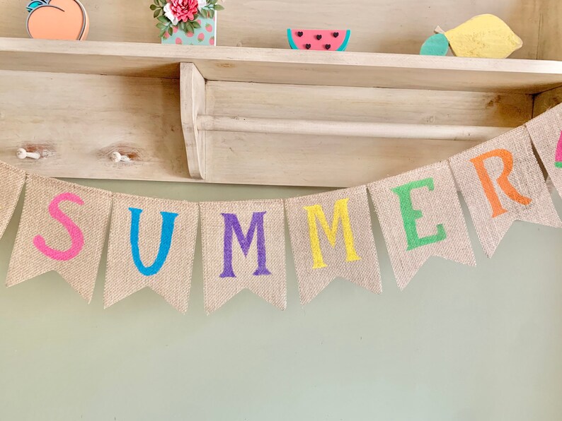 May include: A burlap banner with the word "SUMMER" spelled out in colorful letters. Each letter is a different color: pink, blue, purple, yellow, green, and orange.