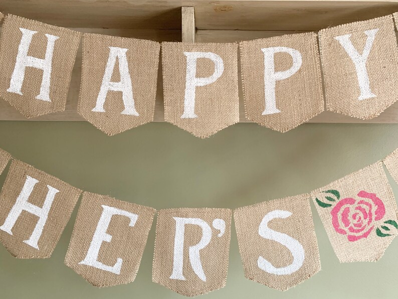 Puede incluir: Una pancarta de arpillera con las palabras "Happy Mother's" pintadas en blanco. La pancarta est&aacute; decorada con una rosa rosa y hojas verdes.