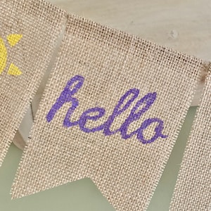 May include: A burlap banner with the word "hello" written in purple paint.