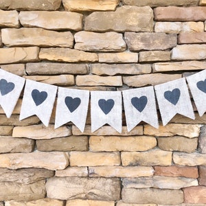 May include: A burlap banner with black heart cutouts. The banner is strung up against a stone wall.
