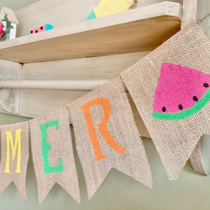 May include: A burlap banner with the word "SUMMER" spelled out in colorful letters. The banner also features a watermelon slice with green and black details.