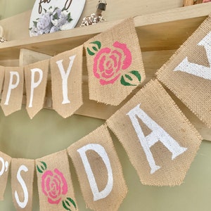 Puede incluir: Una pancarta de arpillera con las palabras "Happy Father's Day" pintadas en blanco. La pancarta est&aacute; decorada con rosas rosas y verdes.
