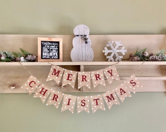 May include: A burlap banner with white polka dots and red lettering that reads "Merry Christmas". The banner is hanging on a wooden shelf with a white wooden snowman, a snowflake, and a small chalkboard sign that reads "Christmas Rules: Be Kind, Build a Snowman, Share Smiles, Believe, Spend Time with Family, Be Jolly".