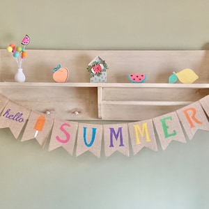 May include: A burlap banner with the word "SUMMER" in colorful letters, along with a sun, ice cream cone, and watermelon. The banner is hanging on a wooden shelf with various summer-themed decorations.