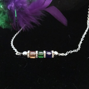 May include: A silver chain necklace with a bar pendant featuring four square-shaped gemstones in shades of orange, green, and blue.