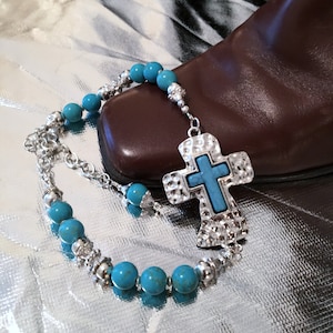 May include: A turquoise and silver necklace with a large, hammered silver cross pendant. The cross has a turquoise stone in the center.