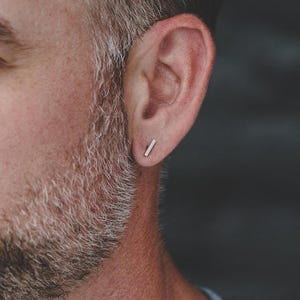 May include: A close-up of a person's ear with a small, silver bar earring.