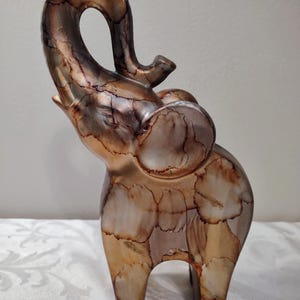 May include: A decorative elephant figurine with an upraised trunk. The sculpture features a metallic finish in shades of gold, bronze, and silver, with a cracked, textured pattern. The elephant is standing on four legs and has large ears.