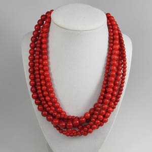 May include: A multi-strand necklace made of bright red beads. The necklace is made of several strands of beads, all of the same size and color.