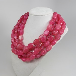 Puede incluir: Un collar de múltiples hilos hecho de cuentas ovaladas de color rosa. El collar está hecho de piedra natural y es una pieza de joyería hermosa y elegante.