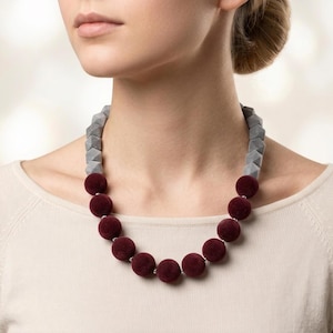 May include: A necklace featuring a series of deep burgundy velvet-textured spherical beads along the bottom half, connected to faceted light grey geometric beads on the upper sides, all strung together on a thin cord around the neck.