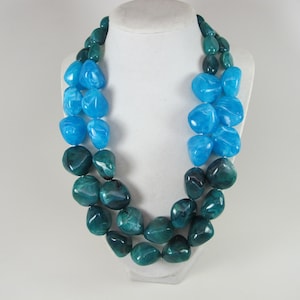 May include: A double-strand necklace made of large, teardrop-shaped beads. The beads are a gradient of blue and green colors.