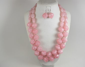 May include: A two-strand pink rose quartz necklace with matching earrings. The necklace features large, faceted, square-shaped beads. The earrings are dangle style with a square-shaped bead.